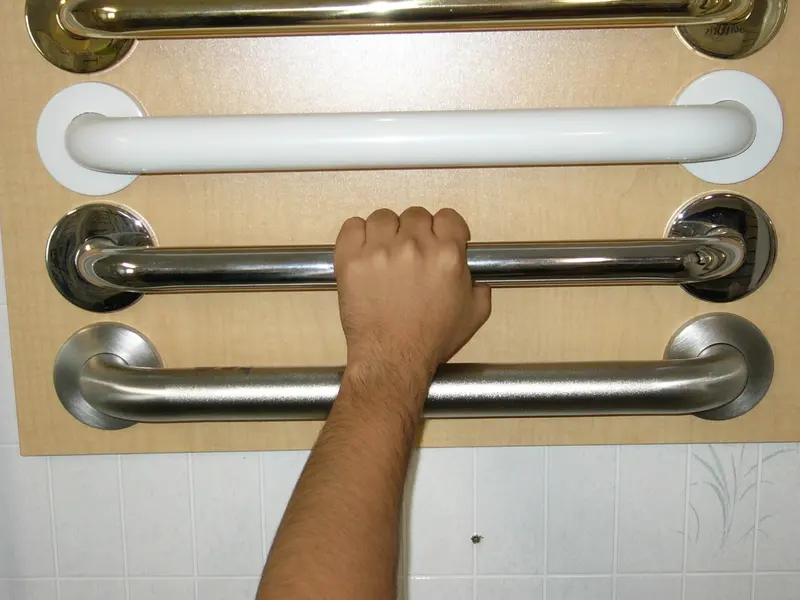 A hand holding one of several metal and white grab rails fixed to a display wall