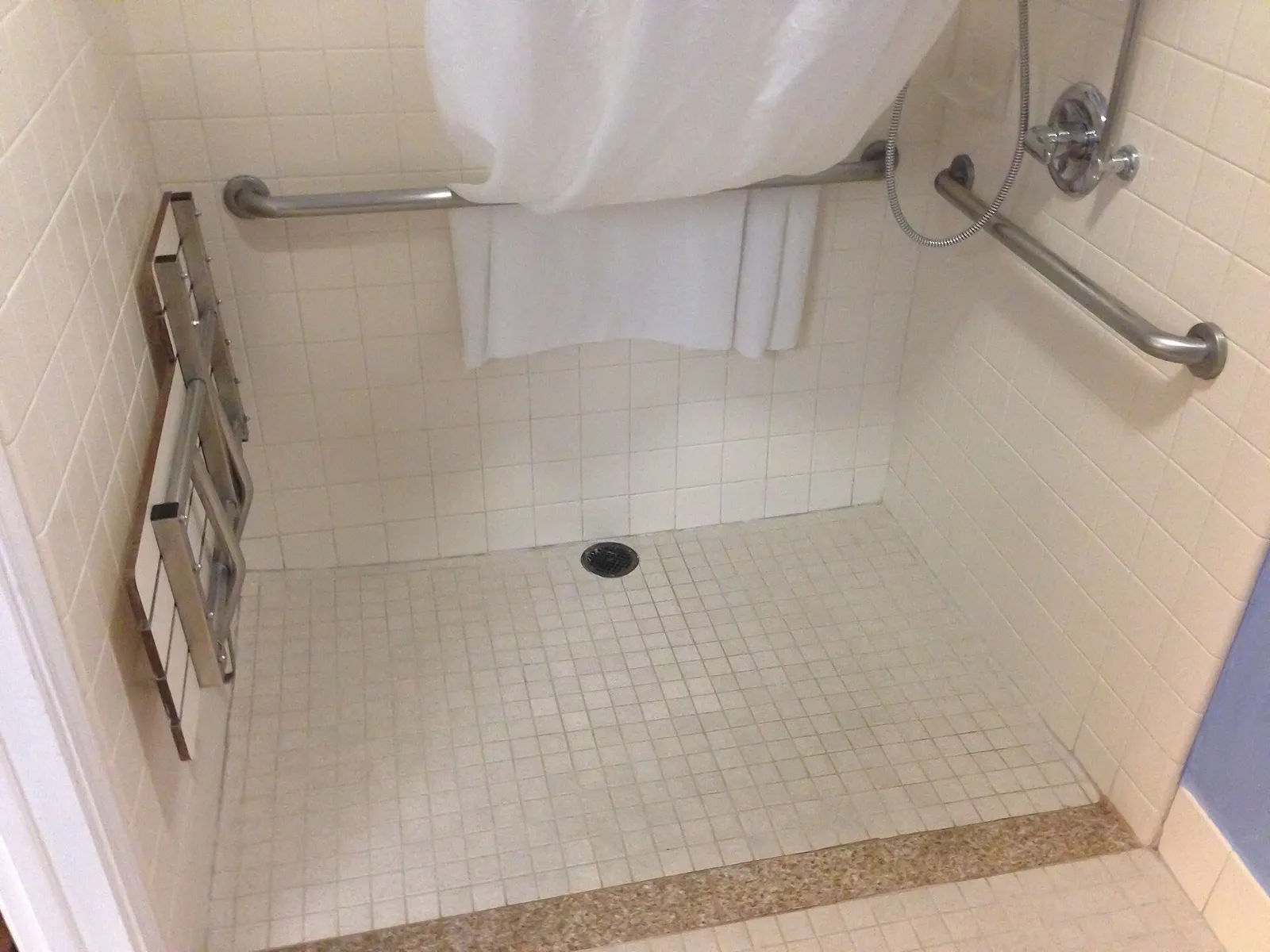 A level-access shower with no step up, a floor drain, a shower curtain and grab rails on the white tiled walls